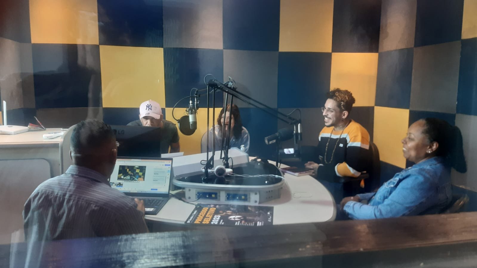 Foto colorida no estúdio da Rádio Comunitária Heliópolis, com João Martins e Mônica Madureiro, colaboradores da SP, e Ana, Reginaldo e Wagner, representantes da rádio e da Unas