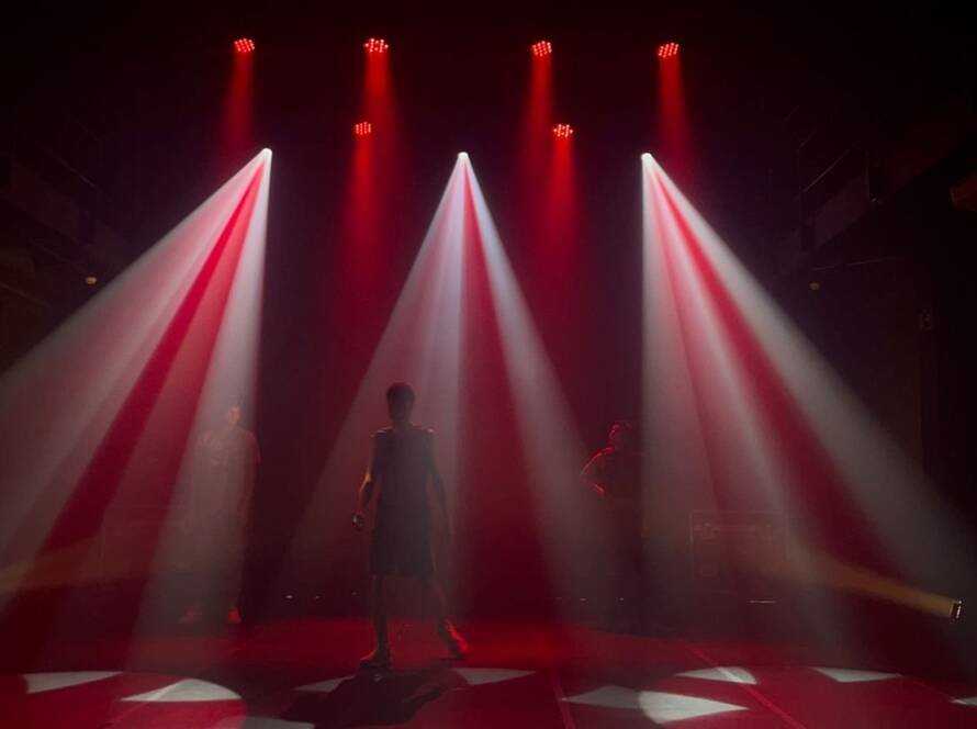 Foto mostrando a combinação da luz vermelha com a branca. Três estudantes da SP Escola de Teatro estão presente