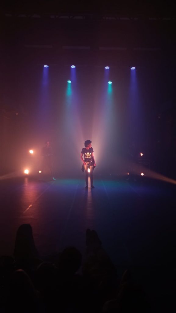 Foto mostrando uma pessoa no palco sob a iluminação das luzes azul e amarela