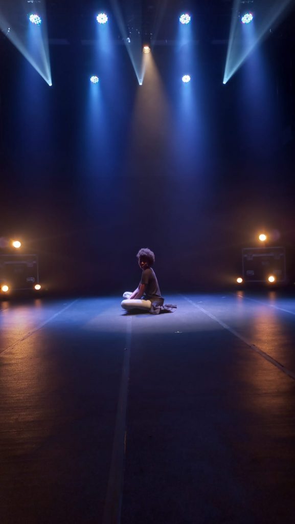 Foto de uma pessoa sentada no palco sob efeito das luzes amarela e azul