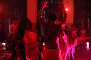 Foto colorida com luz vermelha mostrando estudantes da SP Escola de Teatro em experimento cênico