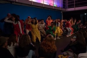 Fotografia colorida mostrando os integrantes do curso de extensão cultural de "Teatro Musical" em apresentação de encerramento