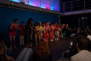 Fotografia colorida mostrando os integrantes do curso de extensão cultural de "Teatro Musical" em apresentação de encerramento