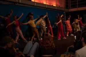 Fotografia colorida mostrando os integrantes do curso de extensão cultural de "Teatro Musical" em apresentação de encerramento