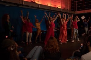 Fotografia colorida mostrando os integrantes do curso de extensão cultural de "Teatro Musical" em apresentação de encerramento