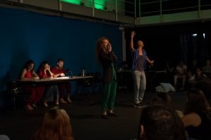 Fotografia colorida mostrando os integrantes do curso de extensão cultural de "Teatro Musical" em apresentação de encerramento