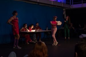 Fotografia colorida mostrando os integrantes do curso de extensão cultural de "Teatro Musical" em apresentação de encerramento