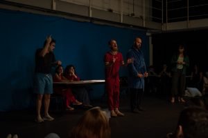 Fotografia colorida mostrando os integrantes do curso de extensão cultural de "Teatro Musical" em apresentação de encerramento