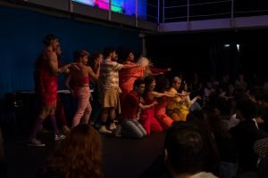 Fotografia colorida mostrando os integrantes do curso de extensão cultural de "Teatro Musical" em apresentação de encerramento