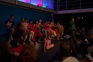 Fotografia colorida mostrando os integrantes do curso de extensão cultural de "Teatro Musical" em apresentação de encerramento