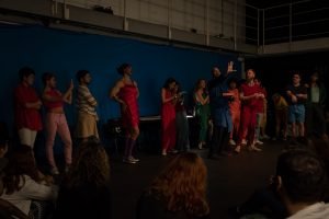 Fotografia colorida mostrando os integrantes do curso de extensão cultural de "Teatro Musical" em apresentação de encerramento