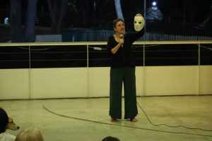 Fotografia colorida mostrando Tiche Vianna falando no microfone e segurando uma máscara