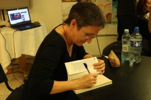 Fotografia colorida mostrando Tiche Vianna autografando o livro