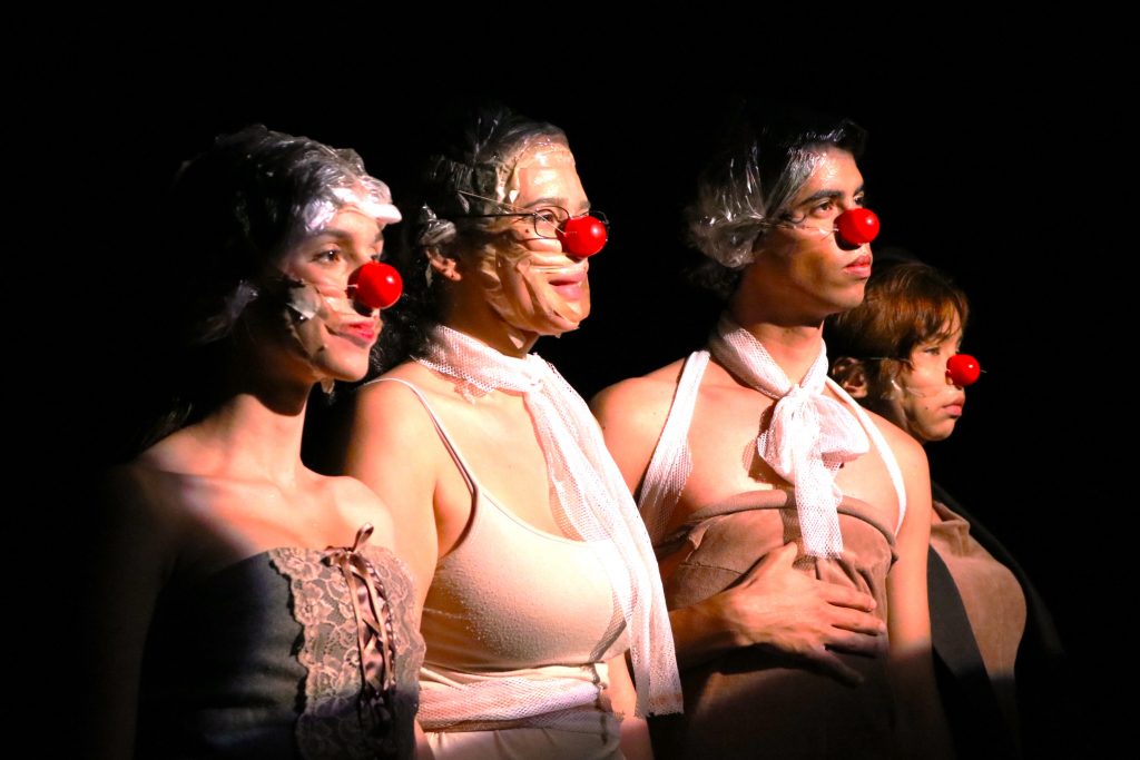 Fotografia colorida mostrando quatro estudantes com nariz de palhaço em experimento cênico