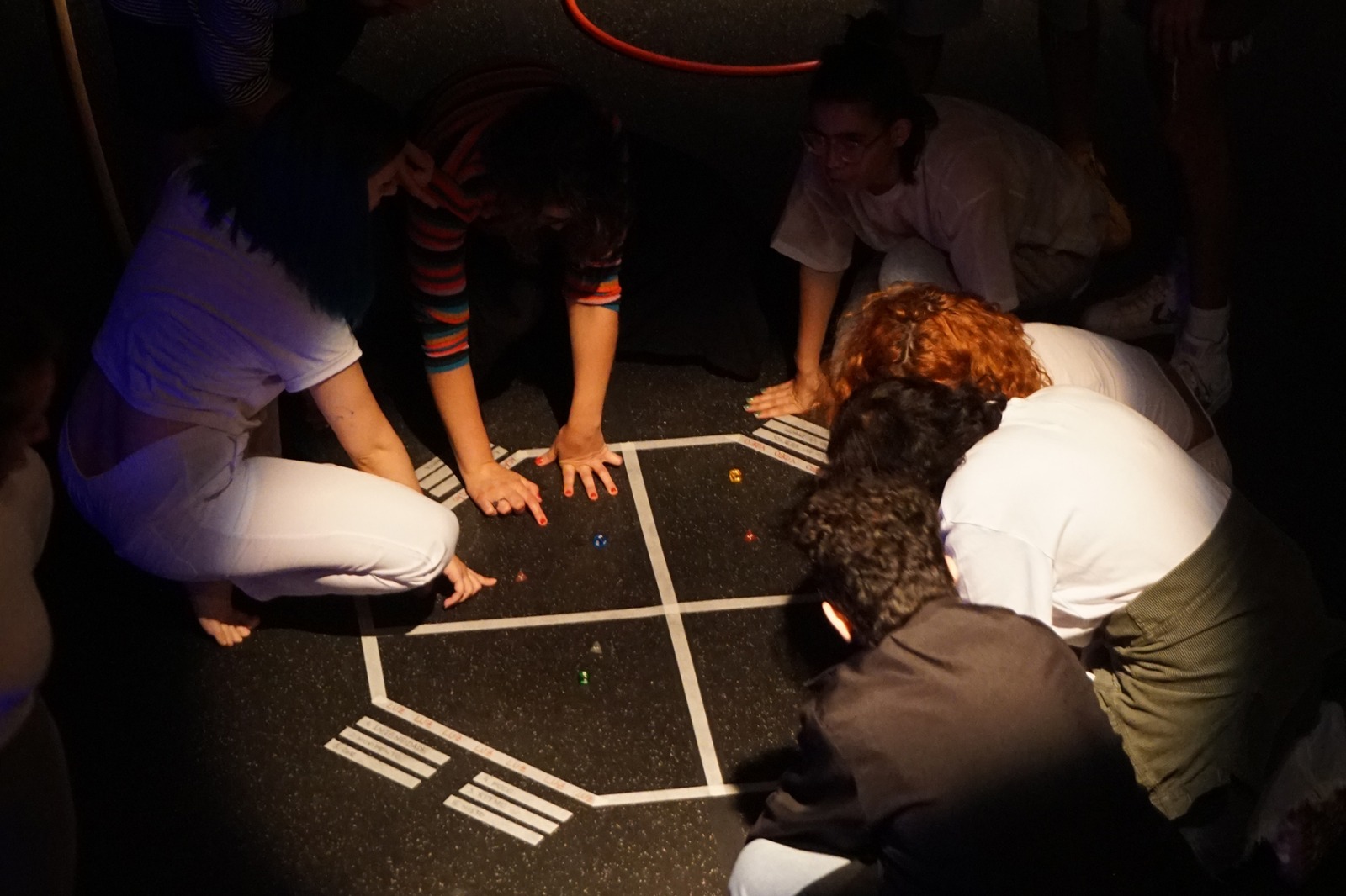 Cena da peça "Geometrias (In)Congruentes", de 2023, com atores com as mãos em um chão preto