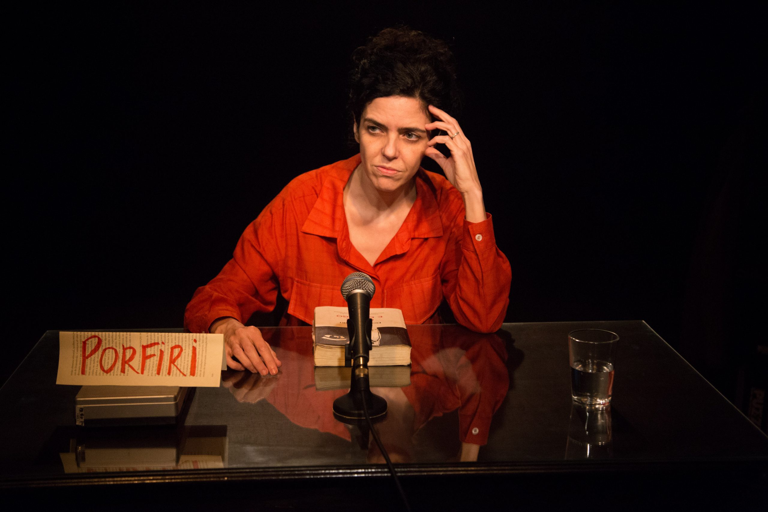 Imagem colorida mostra atriz sentada, em cena, na peça "Crime e Castigo 11:45"