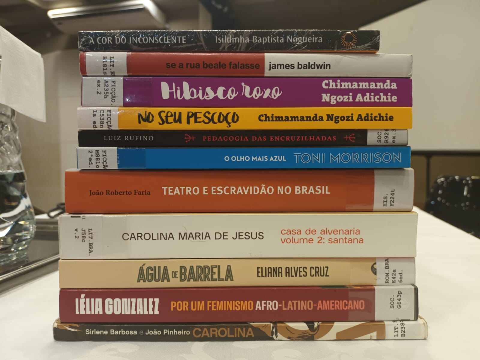 Fotografia colorida de onze lombadas de livros sugeridos pela bibliotecária Monica Madureiro no evento formativo "Letramento Racial"
