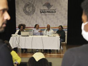 Fotografia colorida da mesa do evento formativo "Letramento Racial" composta por Isildinha, Tâmara, Miguel e Monica