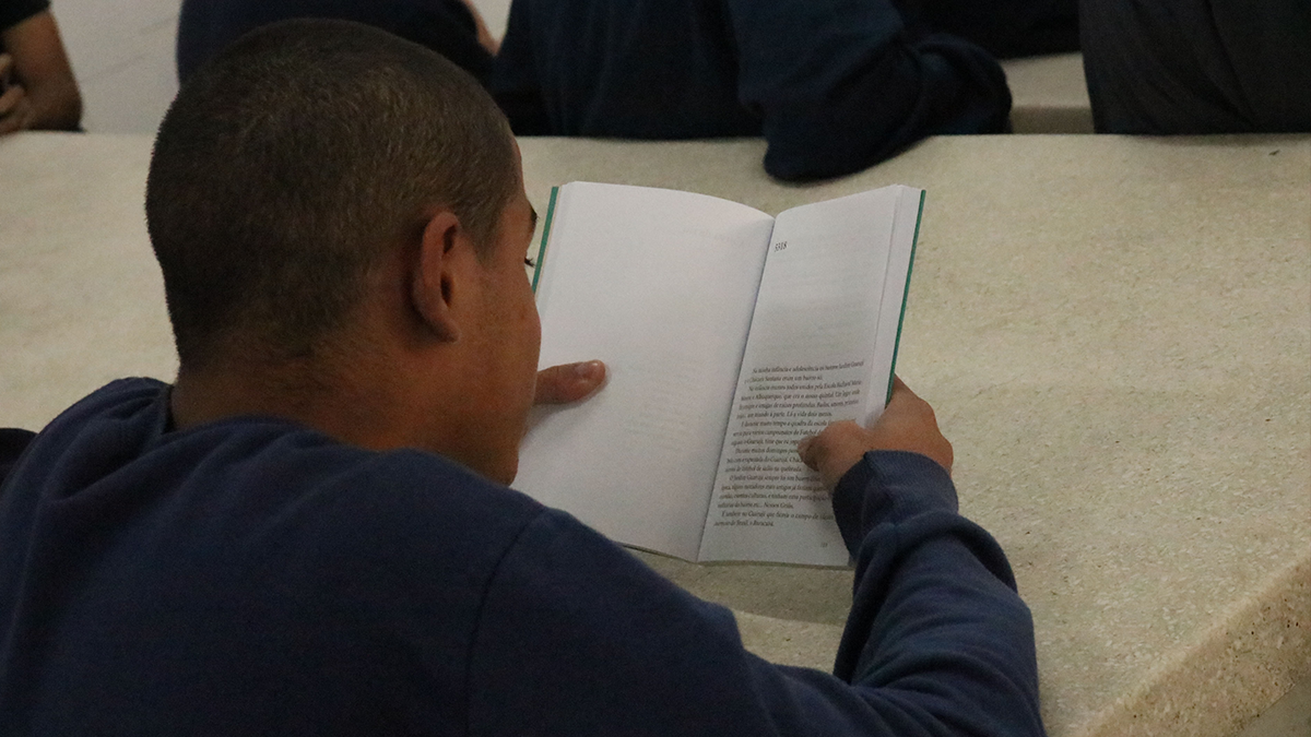 Fotografia colorida de um jovem da Fundação Casa lendo um livro